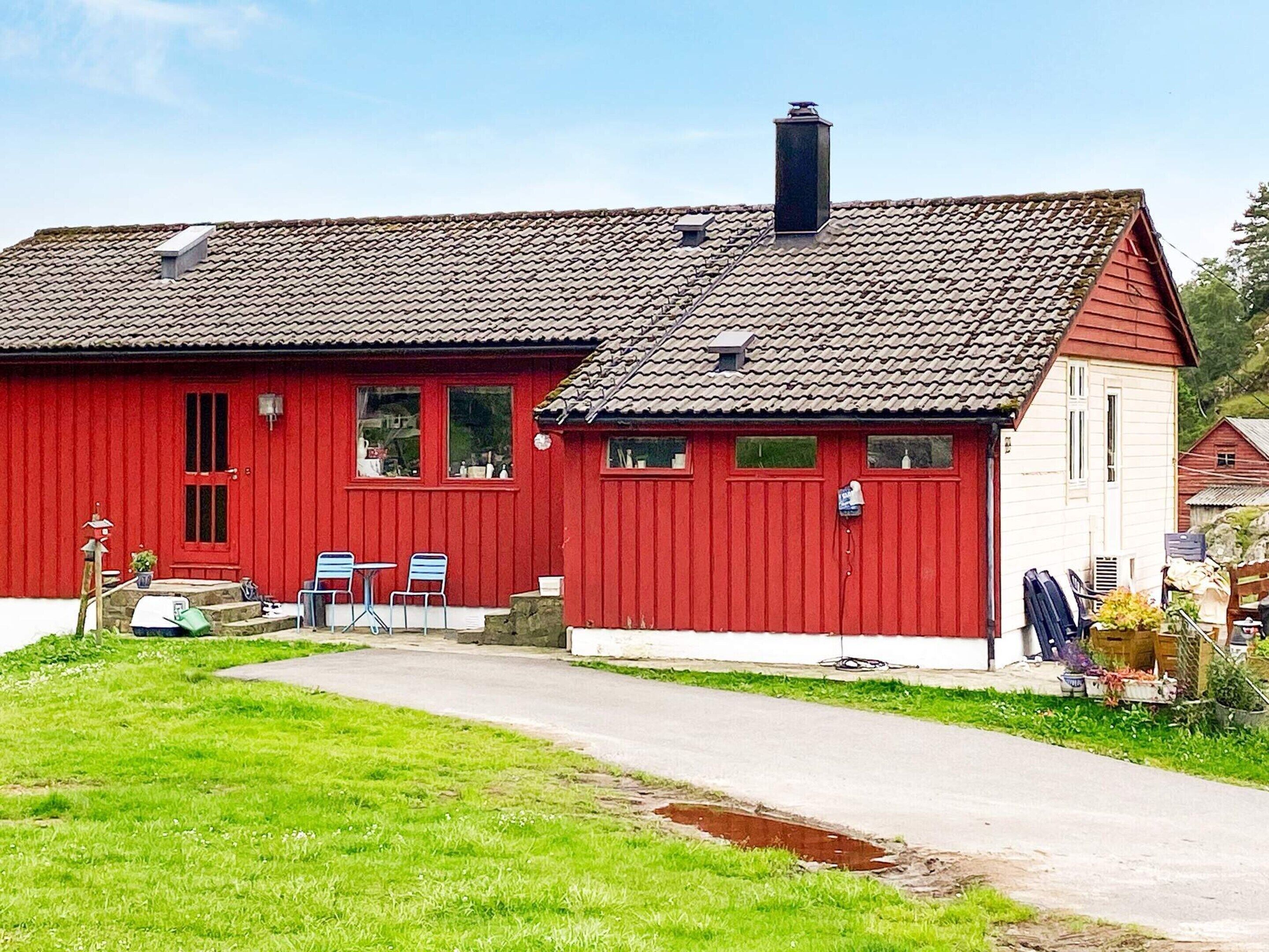 A red building with a tiled roof, a chimney, and a small porch with chairs.