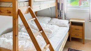 Quarto com beliche, escada de madeira, mesa de cabeceira com gavetas e janela com cortinas.
