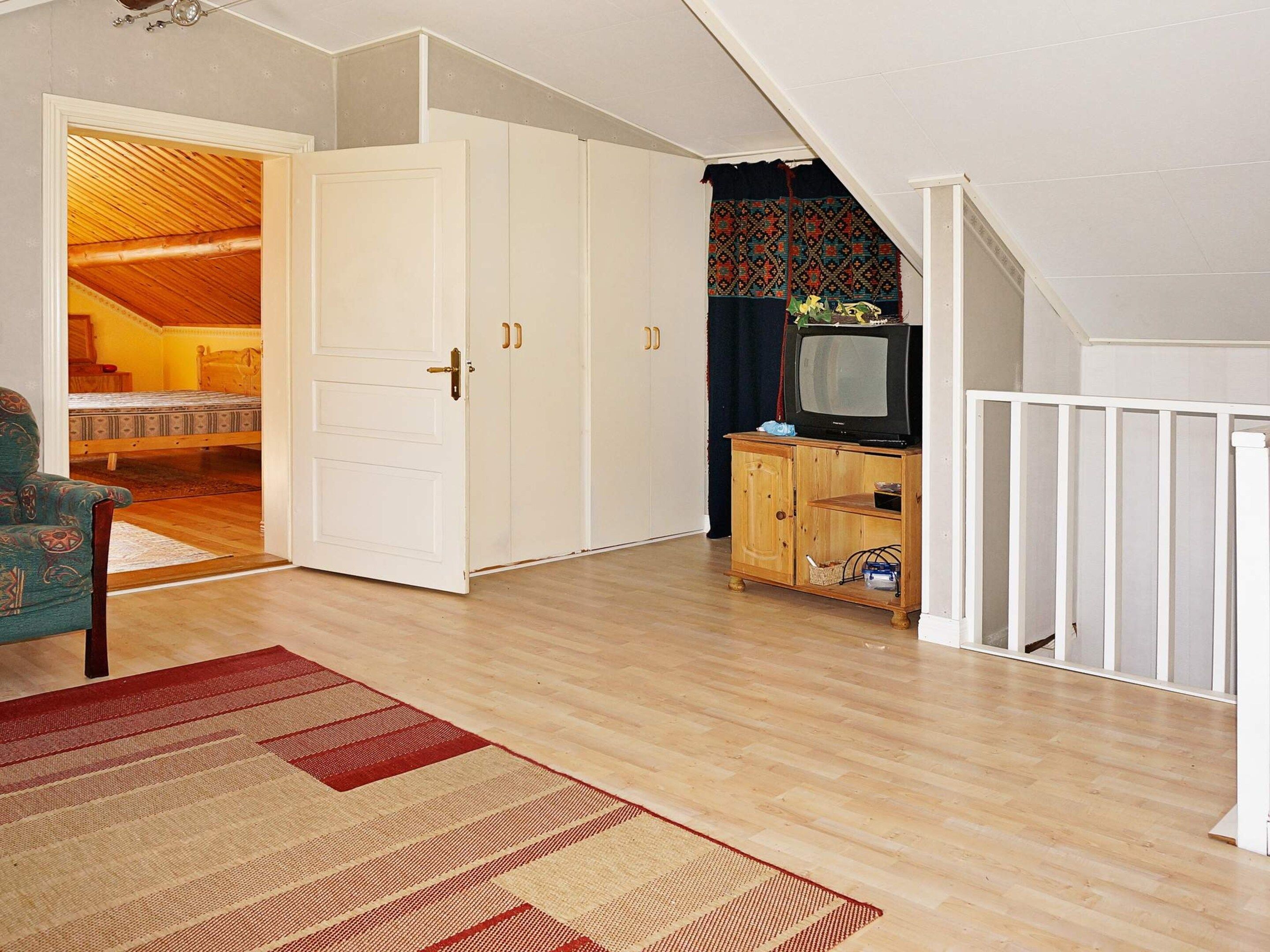 A room with a wooden floor, a television on a wooden cabinet, a door leading to another room, and a patterned rug.