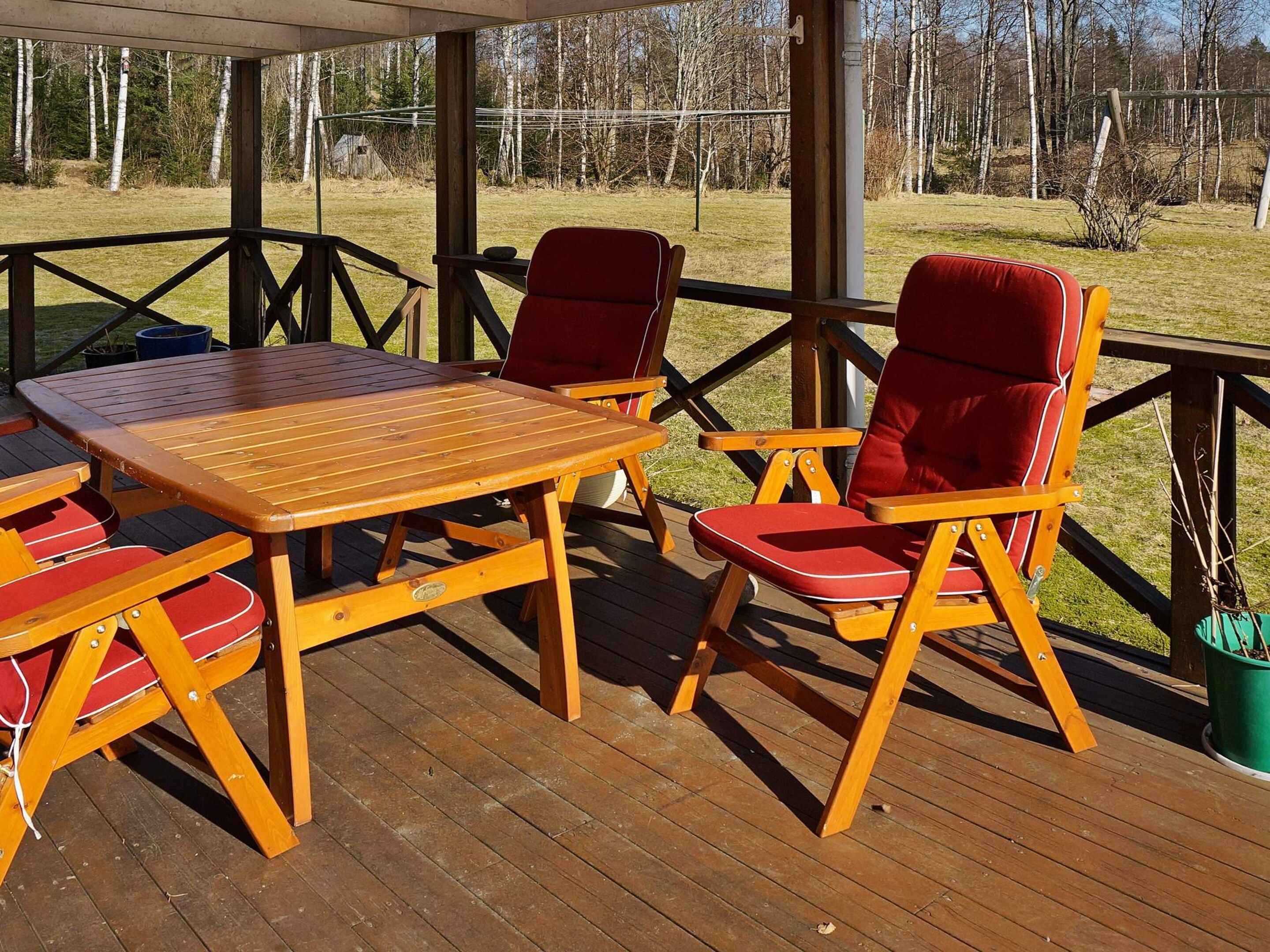 A wooden deck with a table and chairs, a covered area, and a view of a grassy field with trees.