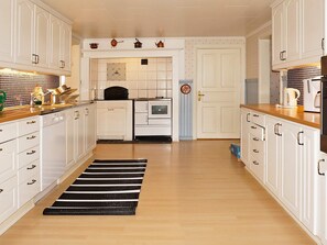 A kitchen with white cabinets, a black and white striped rug, and a door leading to another room.