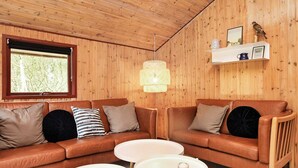 En hyggelig stue med træloft, en lædersofa i brunt, to runde borde i hvidt samt en hængende lampeskærm.