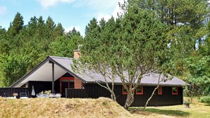 Et moderne hus med saddeltag, en overdækket veranda og et stort træ foran.