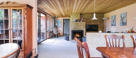 A spacious living area with a fireplace, wooden ceiling, and a dining table with chairs.