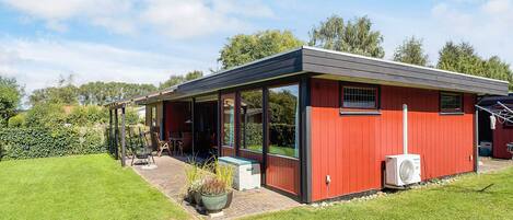 A modern red building with a covered patio, large windows, and a small garden area with potted plants.