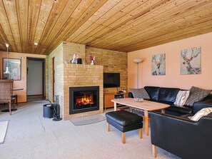 A cozy living room with a fireplace, a black leather sofa, a coffee table, and a brick fireplace surround. - 6 Person Holiday Home in Store Fuglede (Store Fuglede)