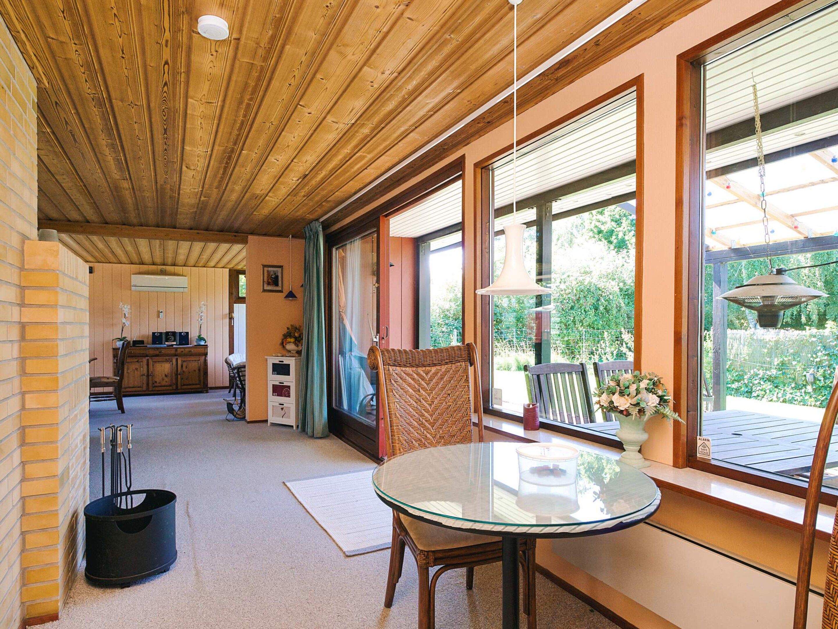 A room with a wooden ceiling, large windows, a glass table, and a chair.