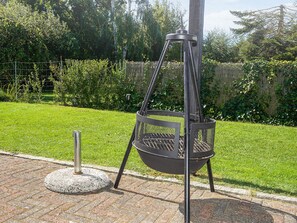 A portable grill with a metal frame and a circular cooking area, placed on a brick surface in a grassy outdoor area. - 6 Person Holiday Home in Store Fuglede (Store Fuglede)