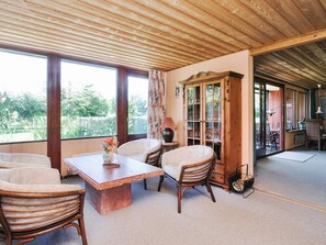 A room with a wooden ceiling, a large window, a dining table, and a cabinet with glass doors.