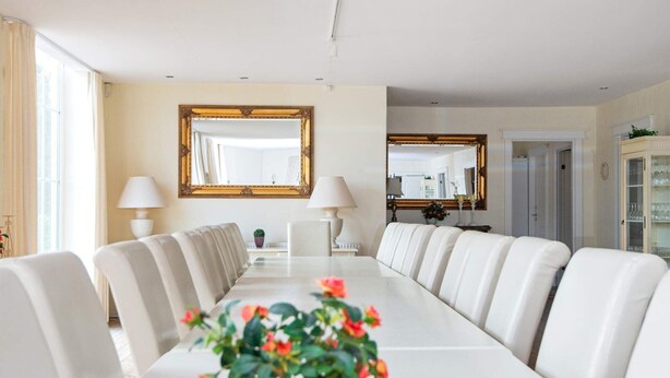 Une salle de conférence avec une longue table, des chaises en cuir blanc et un vase rempli de fleurs.