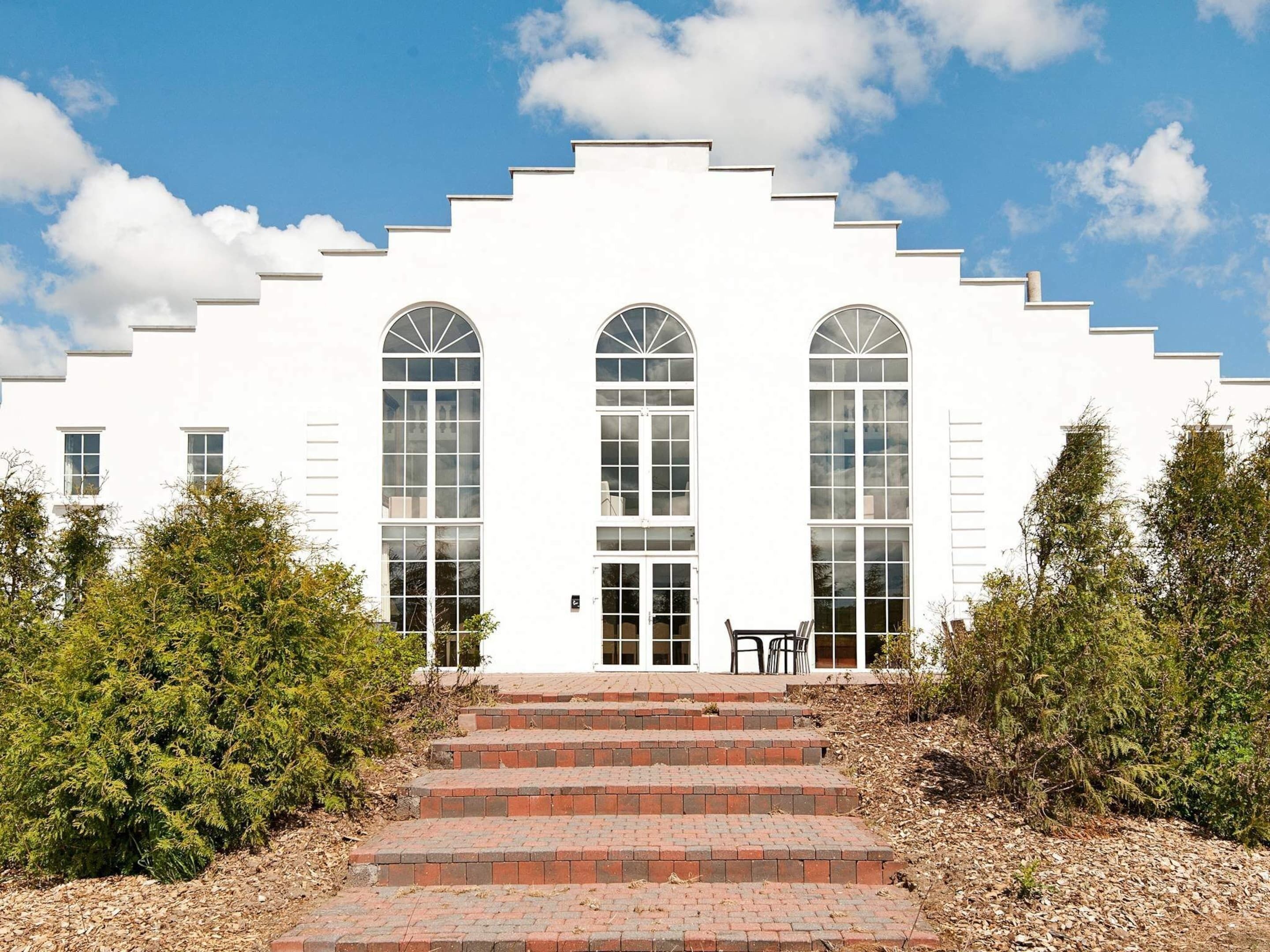 A white building with three arched windows and a set of brick steps leading to the entrance.