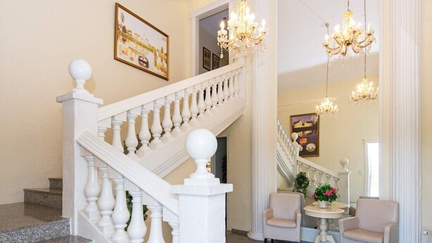 A grand staircase with white balusters and a marble floor leading to a landing area with two chairs and a table, decorated with a chandelier. - 5 Star Holiday Home in Lunderskov (Lunderskov)