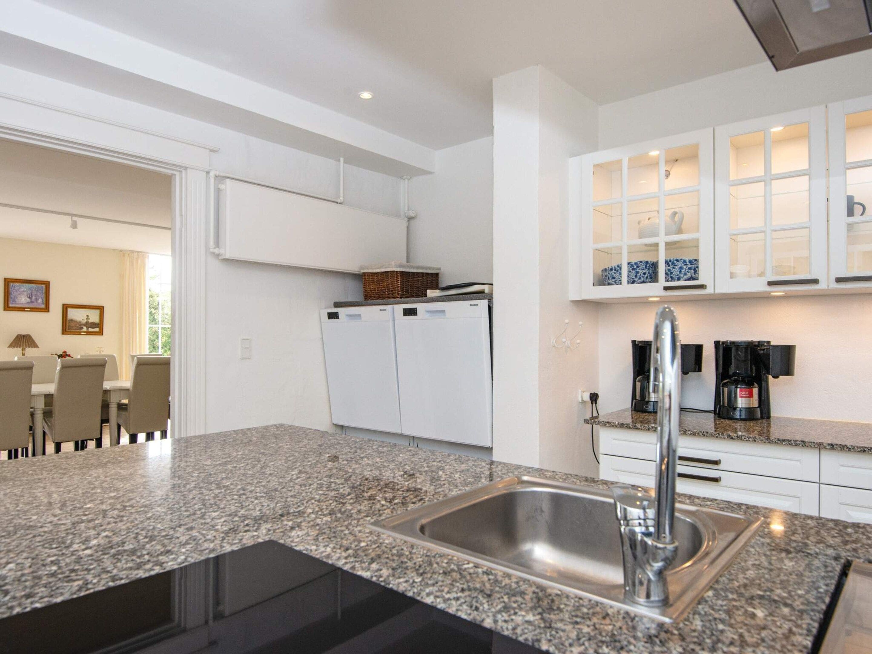Cocina moderna con encimeras de granito, pileta de acero inoxidable y muebles blancos.