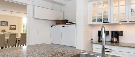 A modern kitchen with granite countertops, a stainless steel sink, and white cabinetry.