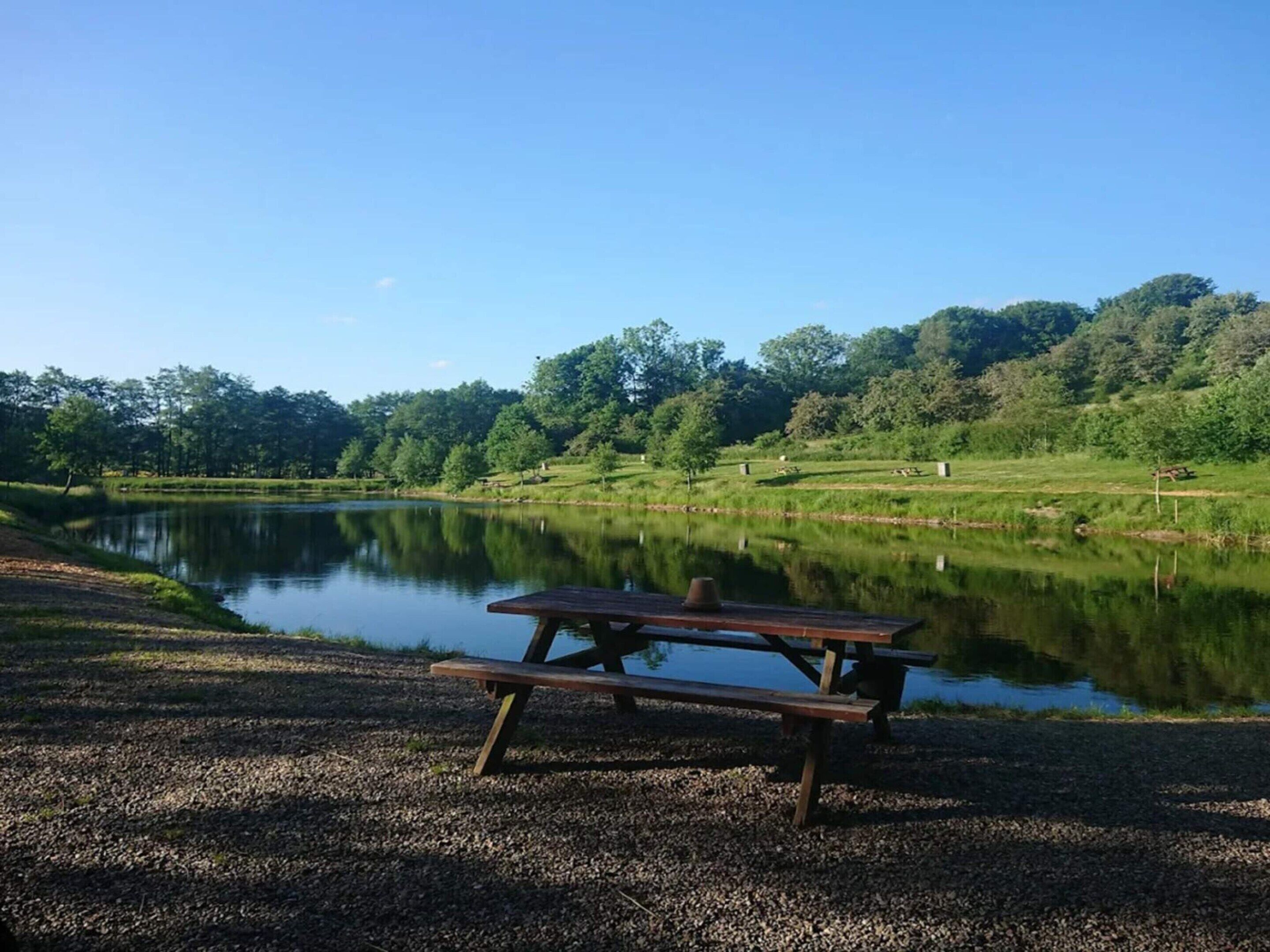 A picnic table by a calm lake with a forested hillside in the background.