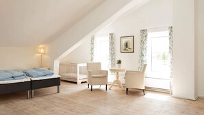 A bedroom with a bed, a crib, a chair, a small table, and a window with curtains. - 5 Star Holiday Home in Lunderskov (Lunderskov)