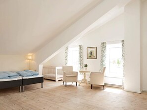 A bedroom with a bed, a crib, a chair, a small table, and a window with curtains. - 5 Star Holiday Home in Lunderskov (Lunderskov)