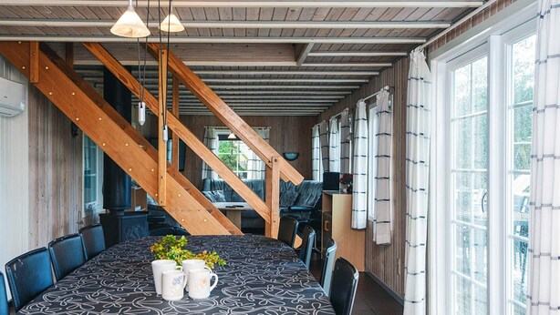 A dining area with a large table, chairs, a staircase, and large windows.