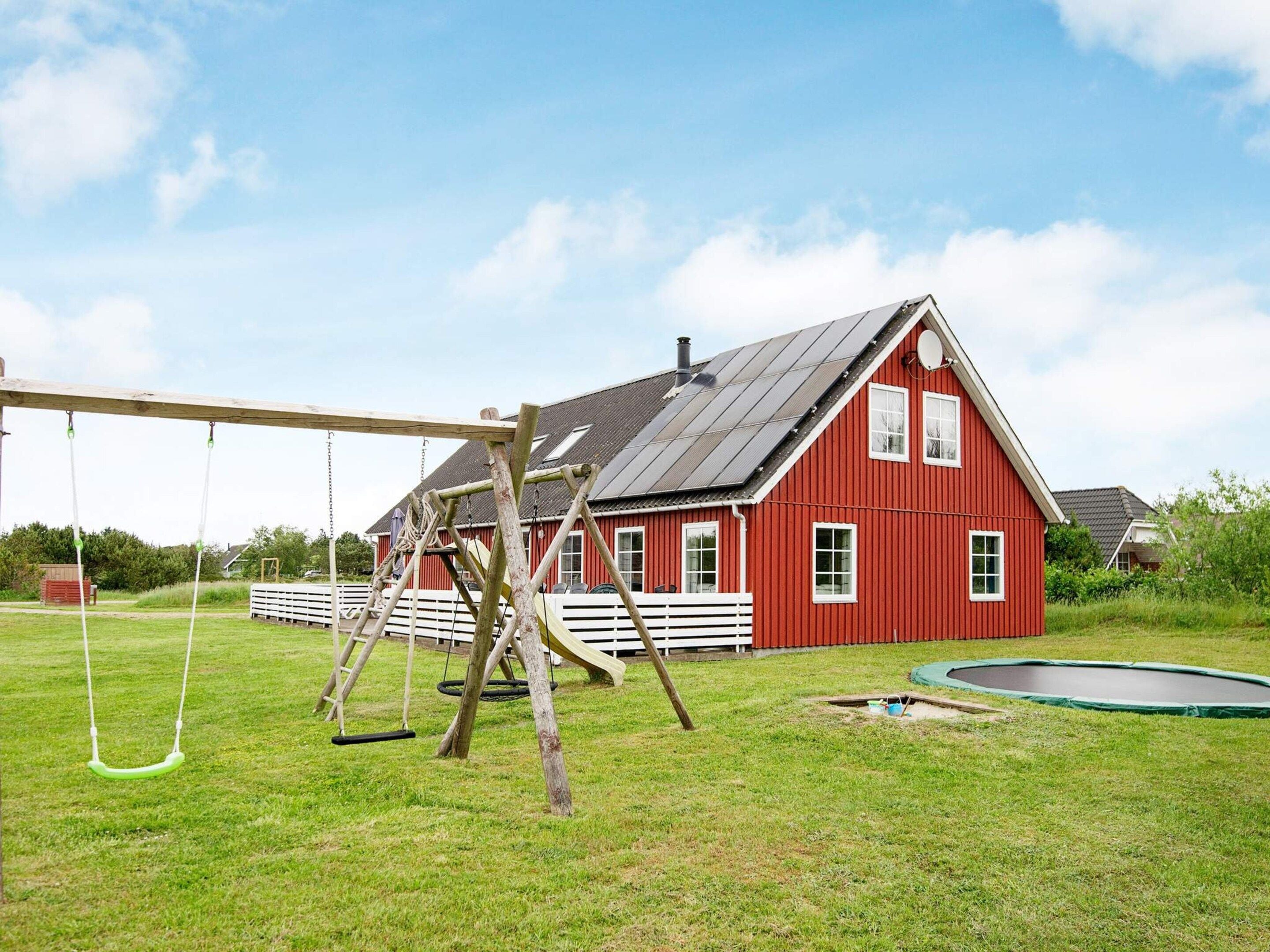 A red barn with a sloped roof, a swing set, and a trampoline in a grassy yard.