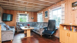 A cozy cabin interior with a wooden ceiling, a sofa, a black chair, a small table, and a bookshelf.