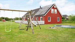A red barn with a sloped roof, a swing set, and a trampoline in a grassy yard.