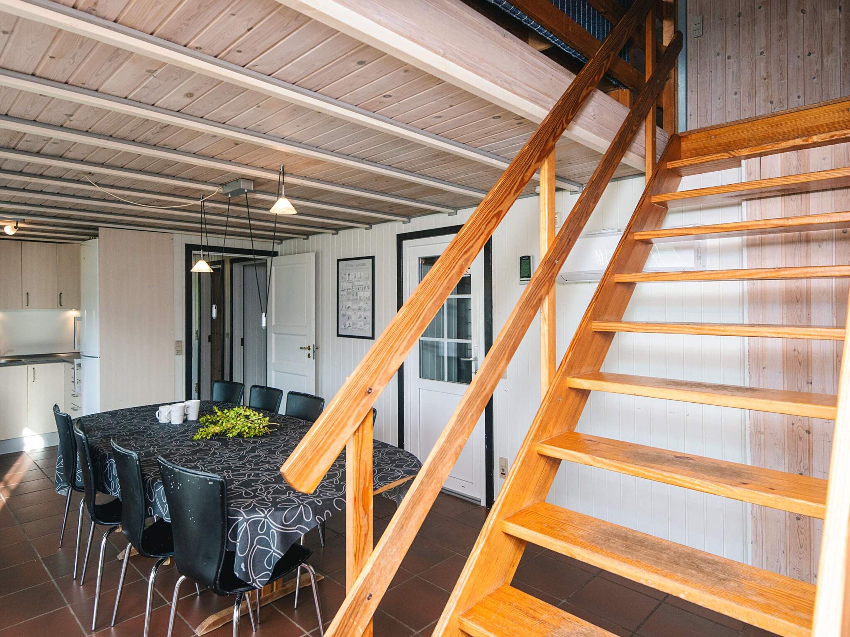 Uma área de refeições com mesa e cadeiras, uma escada e uma cozinha ao fundo.