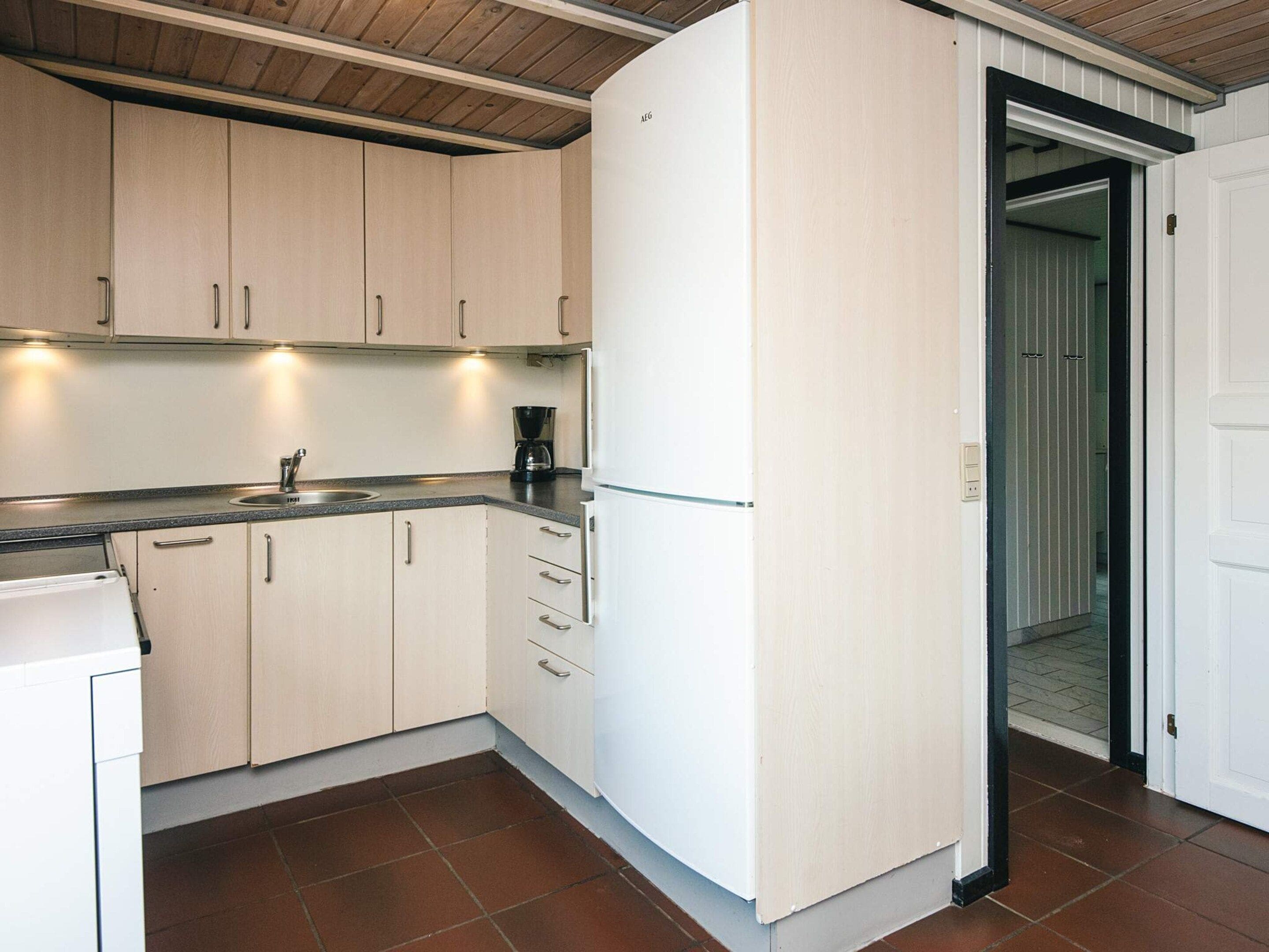 Una cocina con armarios de colores claros, un lavamanos, una cafetera y un refrigerador.