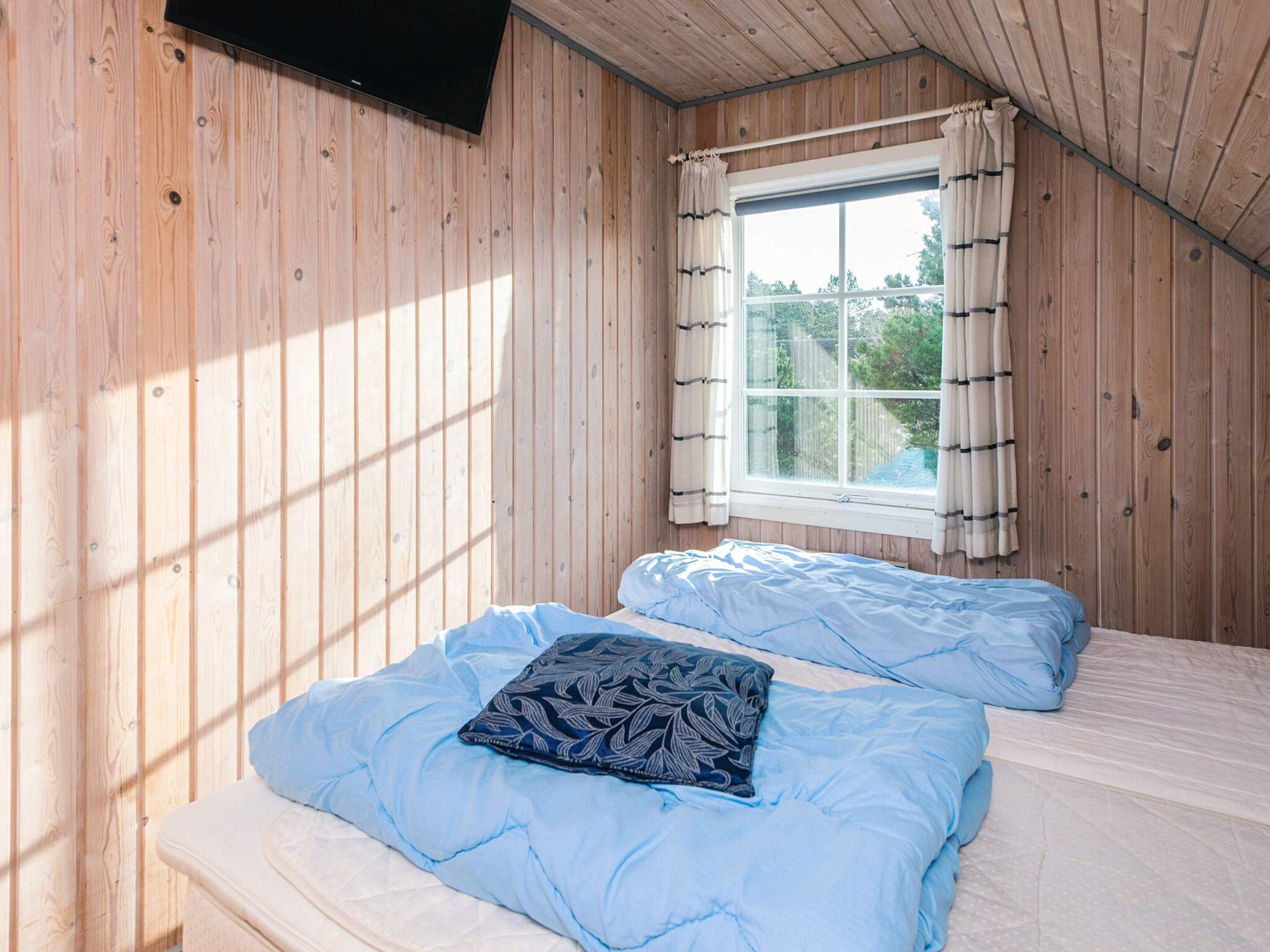 Una habitación con paredes de madera, un ventanal con cortinas y dos camas con ropa de cama azul.