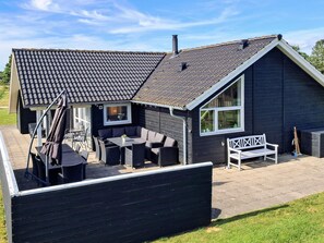 A house with a tiled roof, a patio with outdoor furniture, and a large window.