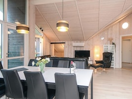 Una sala de estar moderna con comedor, que cuenta con un amplio ventanal, techo de madera y un televisor de pantalla plana.