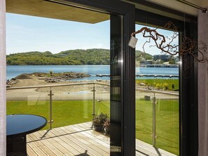 Un balcón con vista a un lago, una terraza de madera y un ventanal de vidrio.