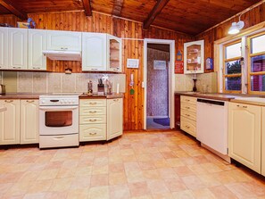 Una cocina con paredes de madera, armarios blancos, estufa y lavavajillas.