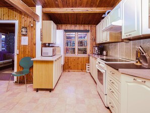Cocina compacta con paredes y armarios de madera, una ventana, un pequeño comedor con una silla y una encimera con un hervidor.