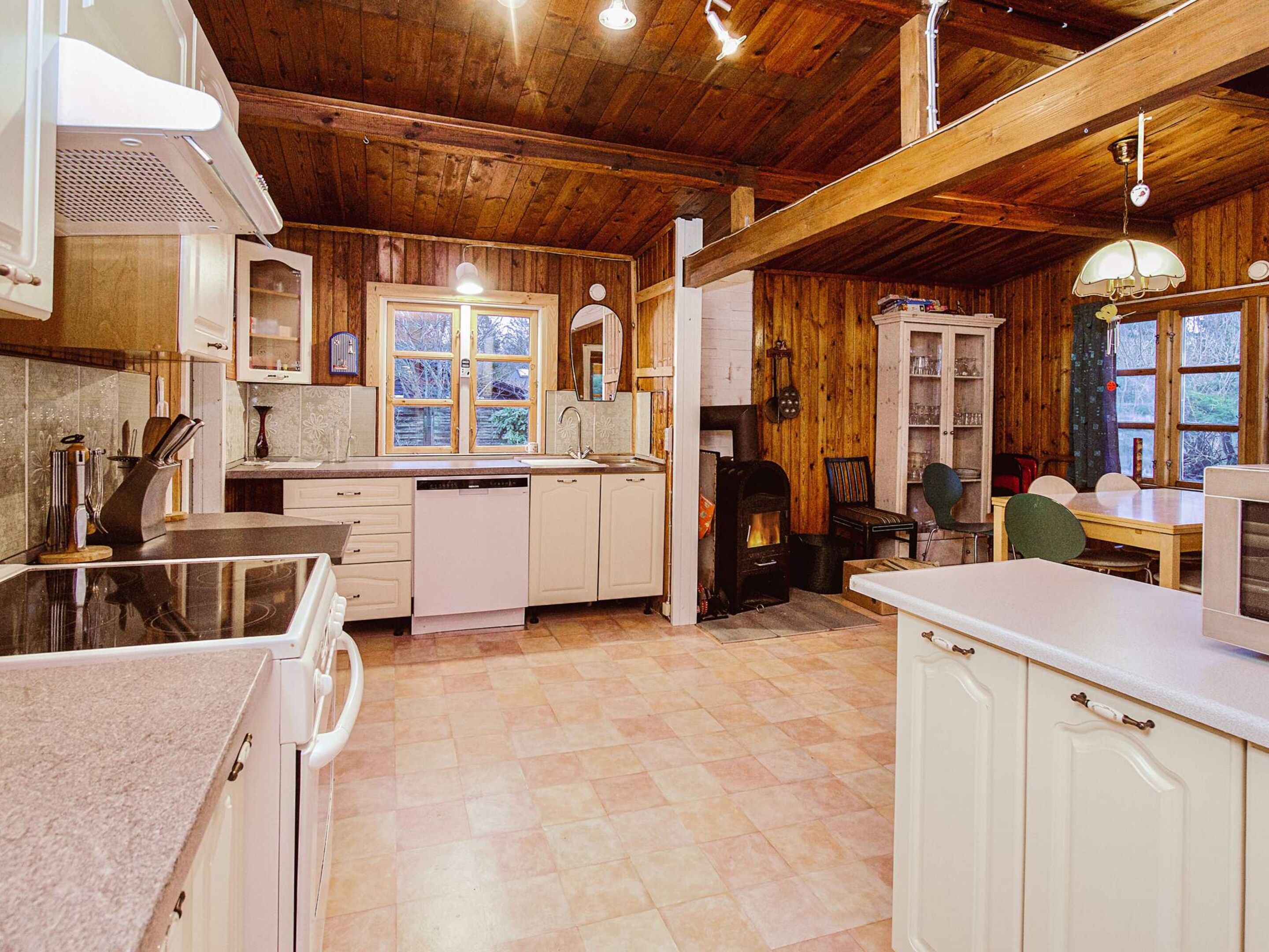Une cuisine avec des poutres en bois, un poêle, des meubles blancs et un coin repas avec une table et des chaises.