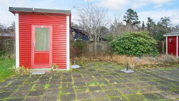 A red shed with a door and window, a paved area with grass patches, and a wooden fence in the background.