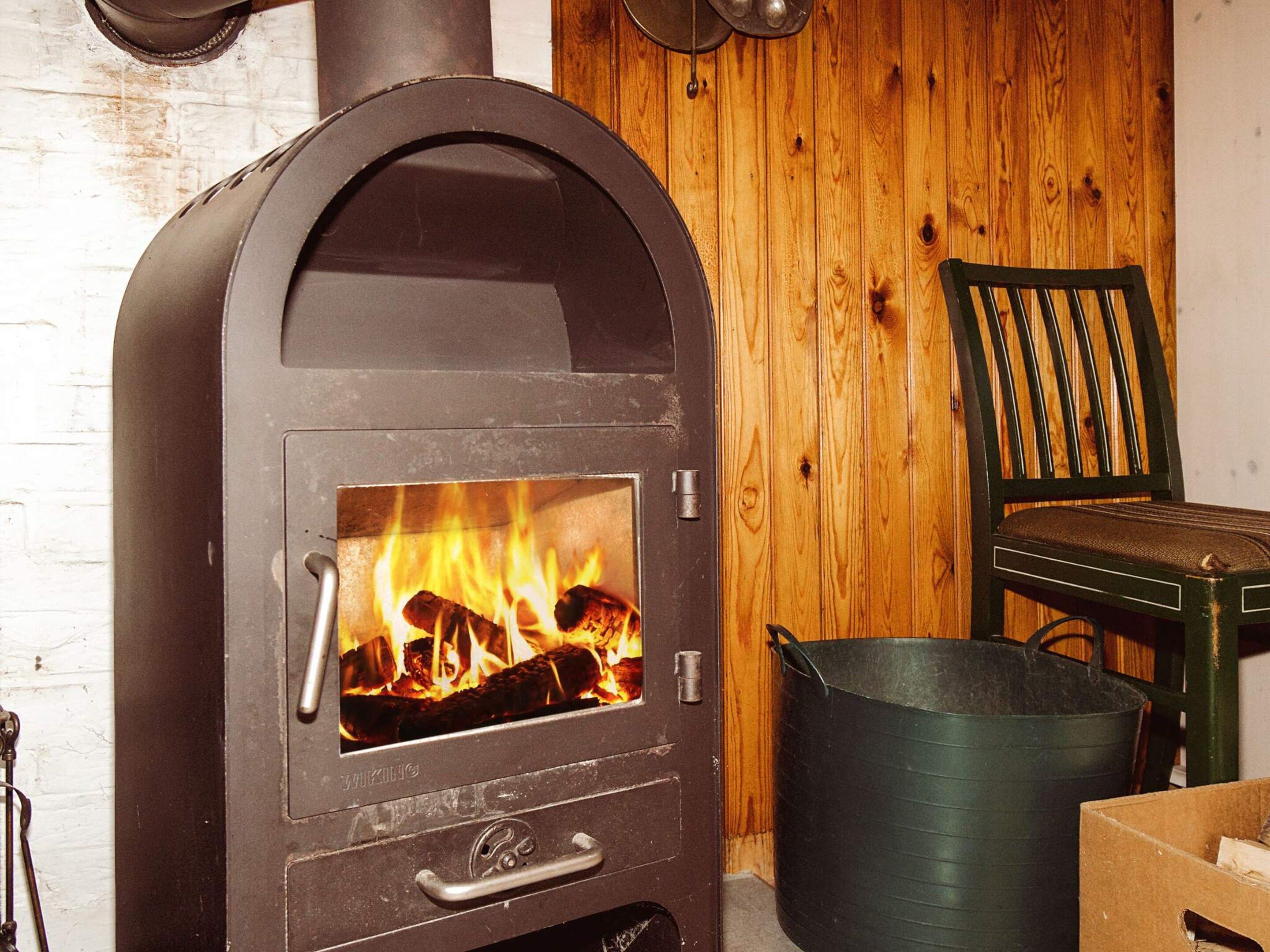A wood-burning stove with visible flames, a green chair, and a metal bucket.