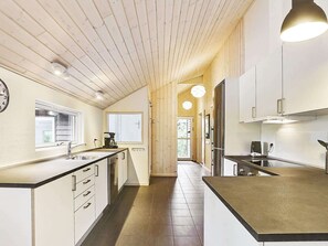 A modern kitchen with wooden beams, white cabinets, a large window, and a built-in oven.