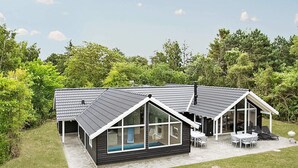 A modern house with a sloped roof, large windows, and a patio area with outdoor furniture. - 5 Star Holiday Home in Tisvildeleje (Tisvildeleje)
