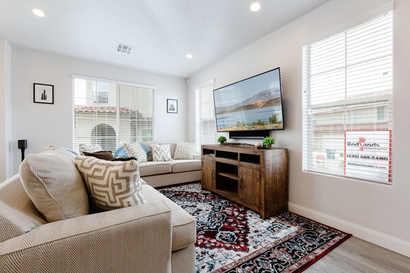 A living room with a sofa, a flat-screen TV, a wooden cabinet, and a patterned rug.