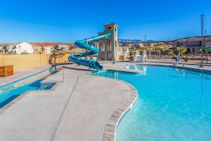 A swimming pool with a blue water slide, a lifeguard tower, and a clear view of the surrounding residential area.