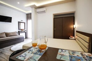 A modern hotel room with a sofa, a table with a pitcher of orange juice, and a bedside table with a candle.