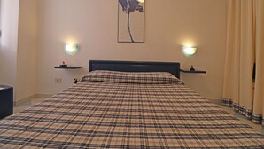 Une chambre à coucher avec un lit, deux tables de chevet, une lampe fixée au mur et un tableau.