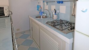 Une cuisine de taille réduite, équipée d’une cuisinière à gaz, d’un évier et de meubles blancs.