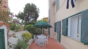 Une terrasse avec une table ronde et des chaises, entourée d’un petit muret en briques et de plantes en pot.