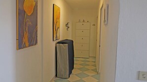 Un couloir avec un sol à carreaux, un radiateur et deux tableaux encadrés accrochés aux murs.