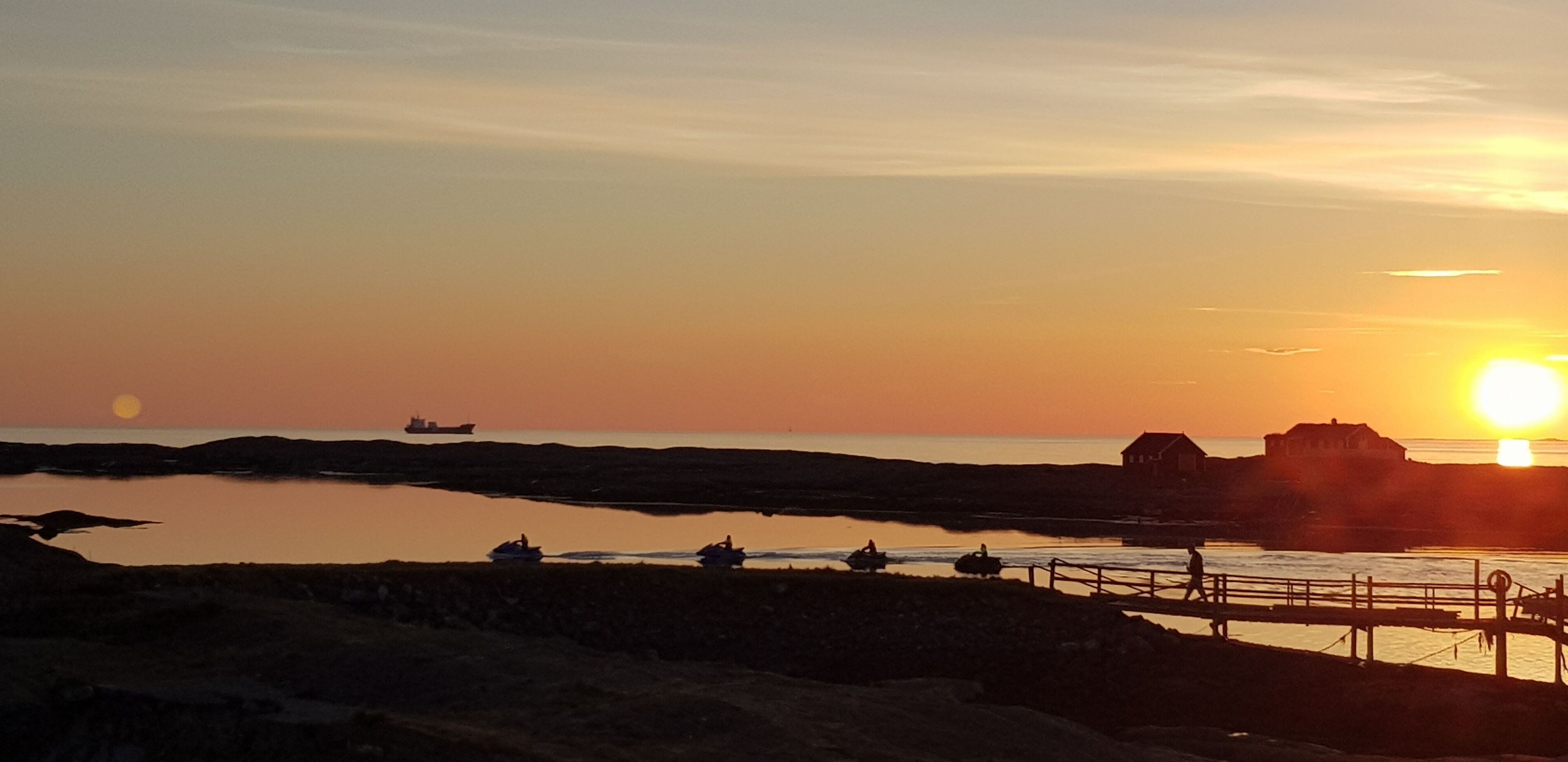 Een zonsondergang boven een kustgebied met boten en een steiger.