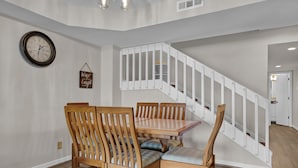 Un coin repas avec une table et des chaises en bois, un escalier blanc et une horloge murale.