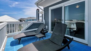 Un balcon avec deux fauteuils et une table, une porte-fenêtre coulissante et une vue sur les maisons voisines.