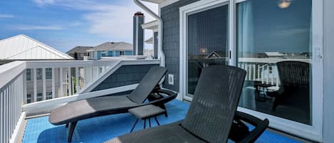 En balkong med två solstolar och ett bord, en skjutdörr i glas och utsikt över de intilliggande husen.