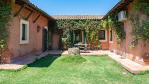 A courtyard with a tiled roof, green shutters, and a stone bench. - Tenuta San Calogero (Augusta)
